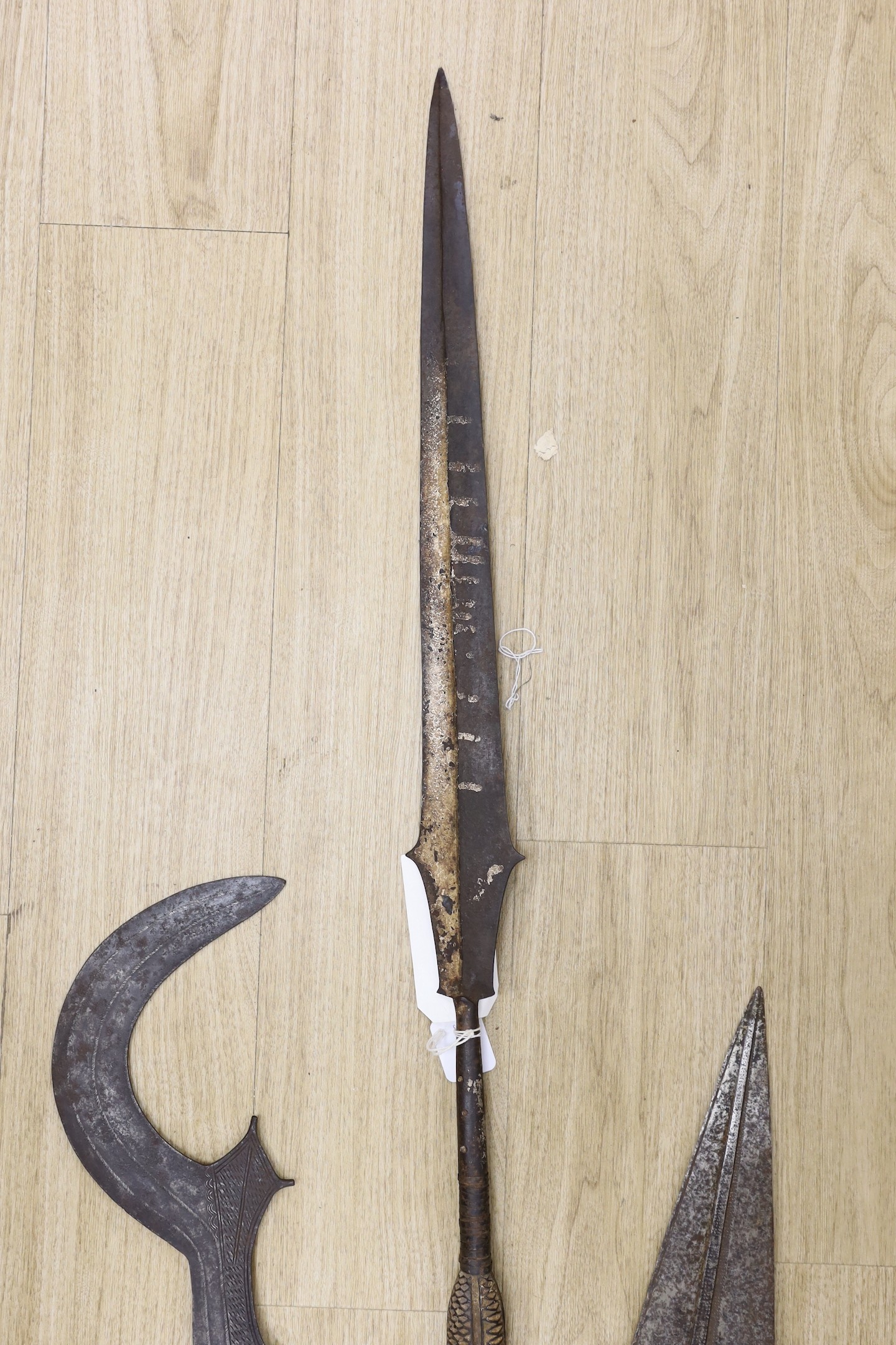 A group of African tribal weapons including an Ngombe ceremonial sword, a similar spear, Democratic Republic of Congo, a Kuba sword and a spear head, spear length 148.5cm